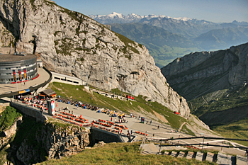 Tiny red cog railway cars climb the final steep slope before reaching the station atop Mount Pilatus Switzerland