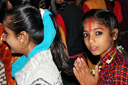 Nepali girl with red tika on her forehead enjoys Bhailo dancers in the streets of Pokhara on day three of the Tihar festival