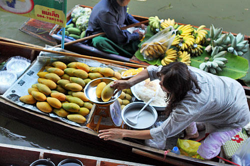 Buying sticky rice and mangoes from a boat vendor at the Damnoen Saduak Floating Market near Bangkok