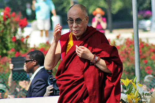 Dalai Lama on stage at the Capitol lawn; photographers and security in the background