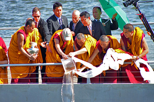 Dalai Lama and monks pour mandala sands into Anacostia River, with Potomac in background