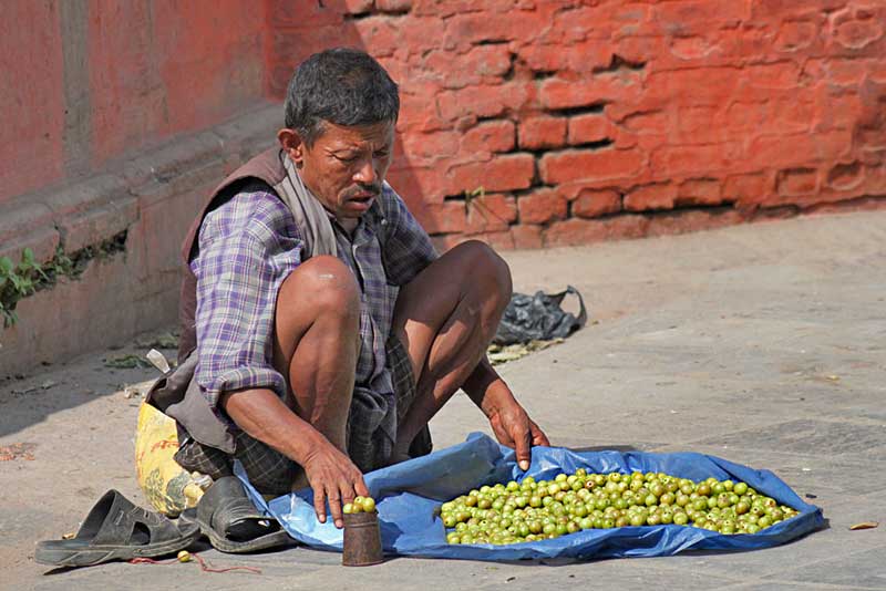 Poor Farmer Squats in Durbar Square in Kathmandu, Nepal to Sell His Small Pile of Fruit