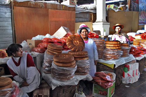 Quechua women at San Pedro Market in Cusco stand aside stacks of bread rounds