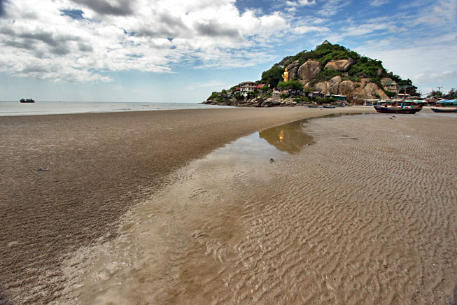 Golden Buddha on Khao Taiab hill reflects in puddle during low tide on Takiab Beach