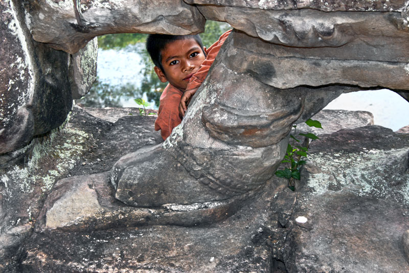 Boy Peeks From Behind Giant Carvings at Angkor Wat Ruins in Siem Reap, Cambodia