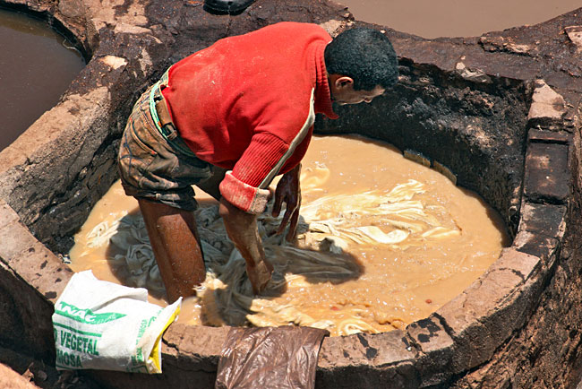 Worker moves hides in a dye vat around with his feet and hands