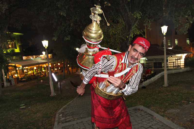 Istanbul Sherbet Vendor in Traditional Costume Pours Drink from a Large Vessel Carried on his Back