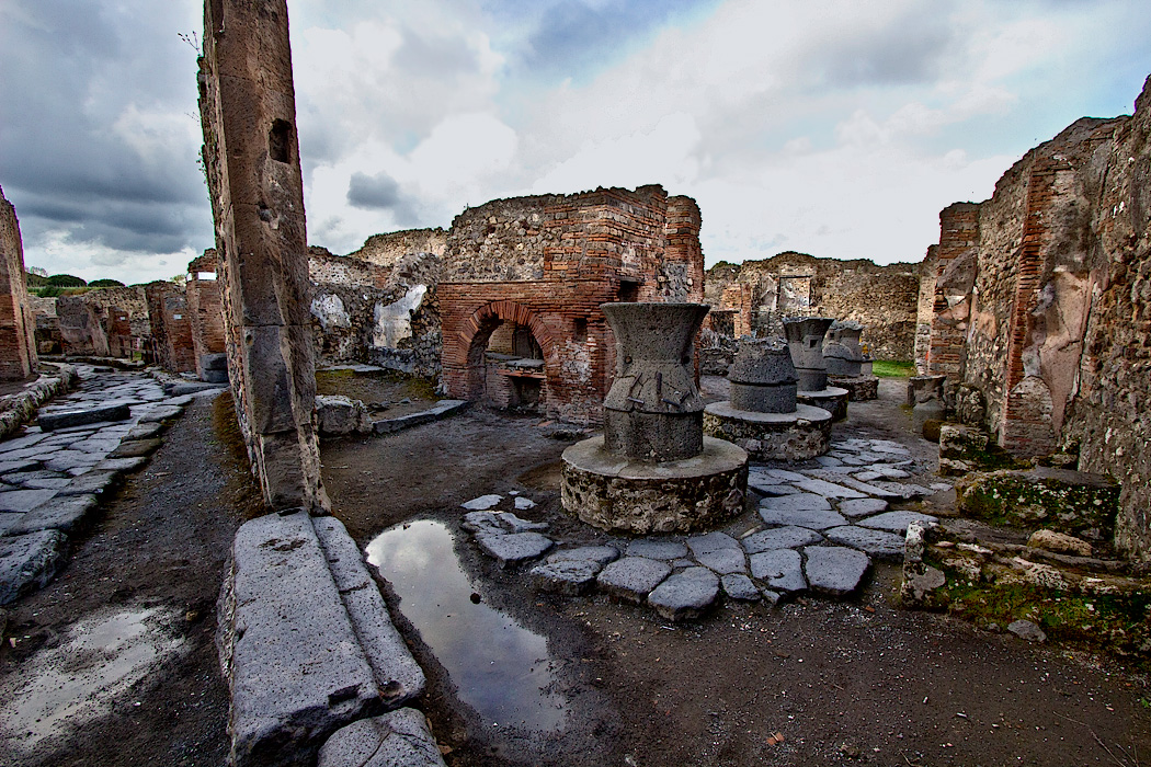 Ruins of large bakery at Pompeii, Italy, with remains of exterior wall and street leading up to the shop