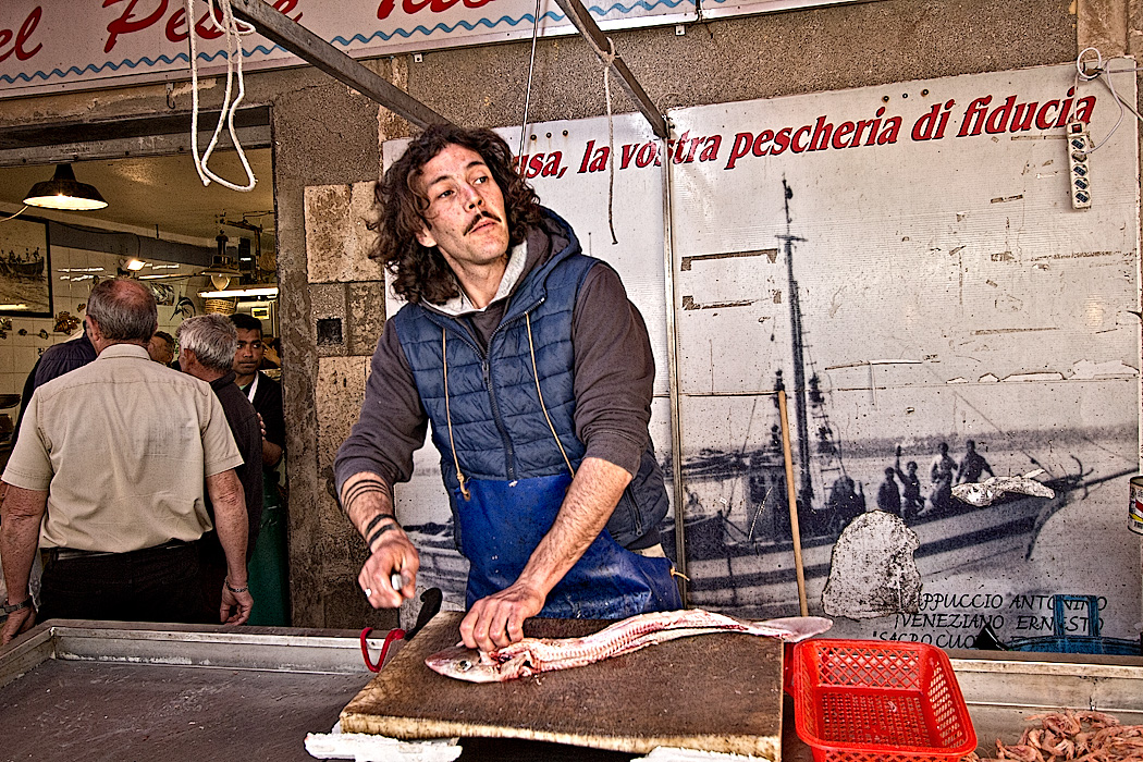 Fish monger prepares fresh-caught seafood at the daily morning market in Syracuse, Sicily.