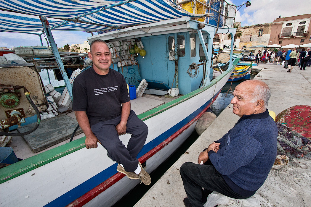 Local men take a break from the Sunday market in Marsaxlokk, on the island of Malta