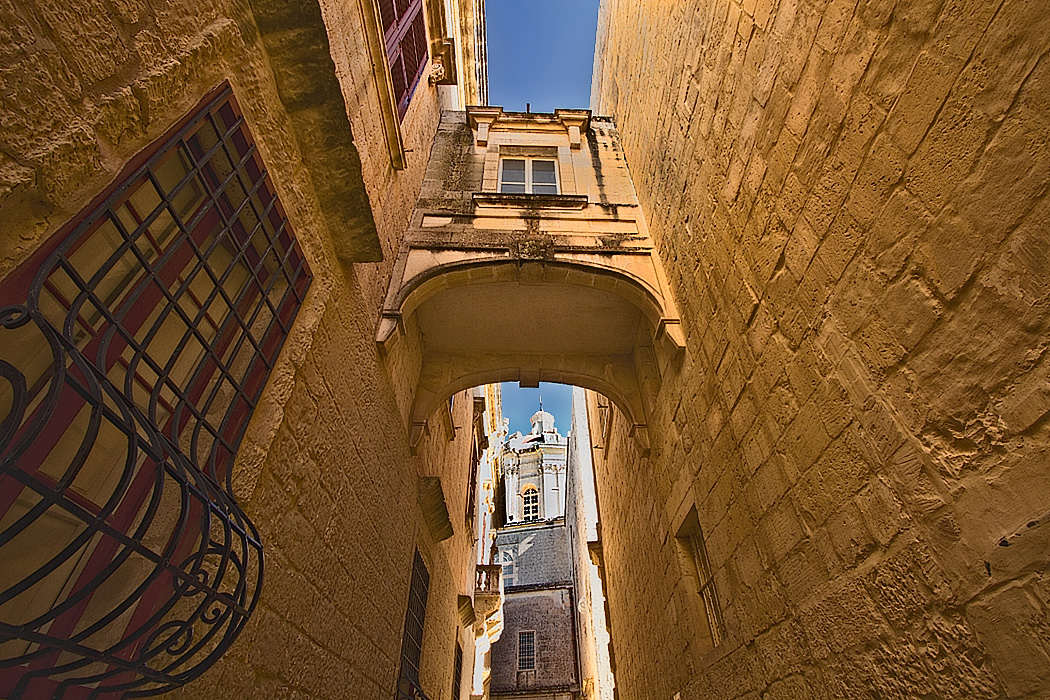 Stone bridge between buildings frames St. Paul's Cathedral in the old walled city of Mdina on the island of Malta