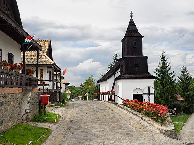 Main street in the historic center of Holloko leads past adobe houses with stone foundations, to the wooden-steepled church