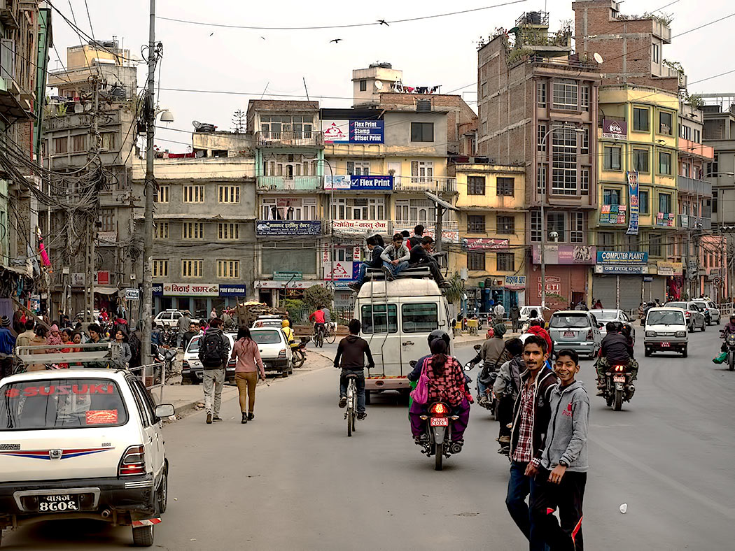 Typical street scene in Kathmandu, Nepal, with people riding on the roof of overloaded van bus