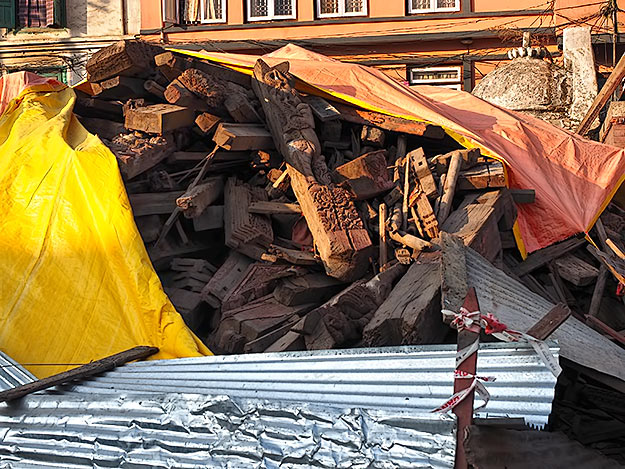 A pile of ancient wooden carvings lies covered with a tarpaulin, awaiting government plans for reconstruction