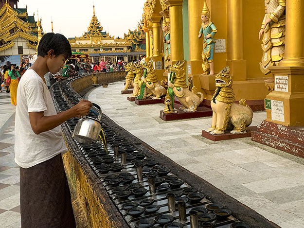 Worker at Shwedagon Pagoda in Yangon, Myanmar, refills oil lamps that surround the main spire