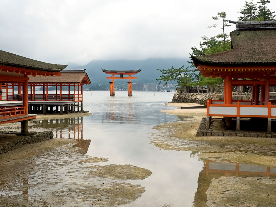 As the tide rolls in toward Itsukushima Shrine, water floods over the massive wooden legs of Torii Gate on Miyajima Island, just across the bay from Hiroshima, Japan
