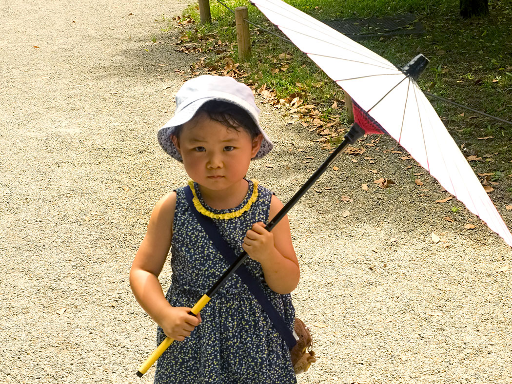 Japanese girl with umbrella shelters from the sun in Hama-rikyu Gardens in Tokyo, Japan