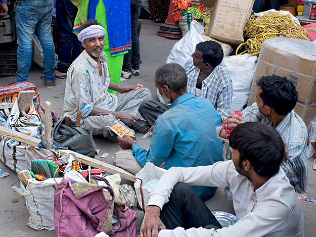 Workers sit cross-legged in the streets of Delhi India, tools at the ready, hoping to be hired for day work