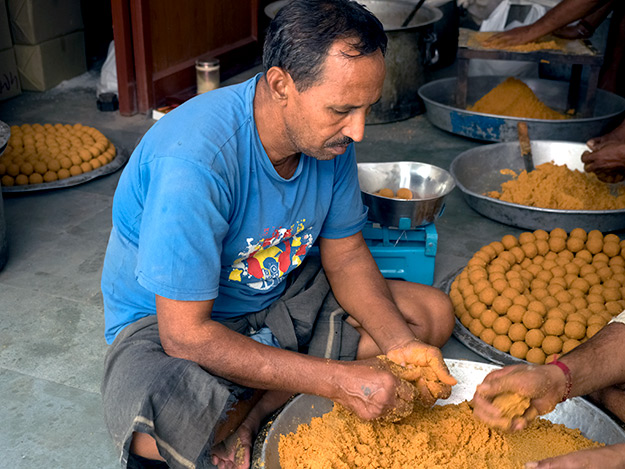 Men roll out Besan Ladoo balls made of ground chickpeas, sugar and ghee
