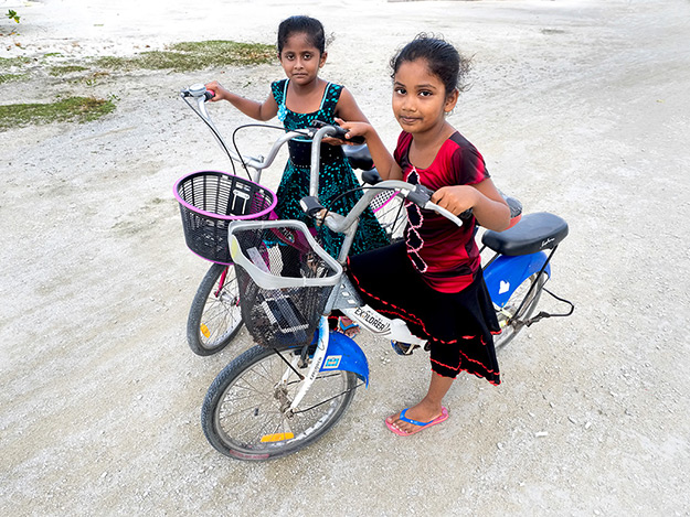 Two young girls on Bodufolhudhoo cycle around the sand streets