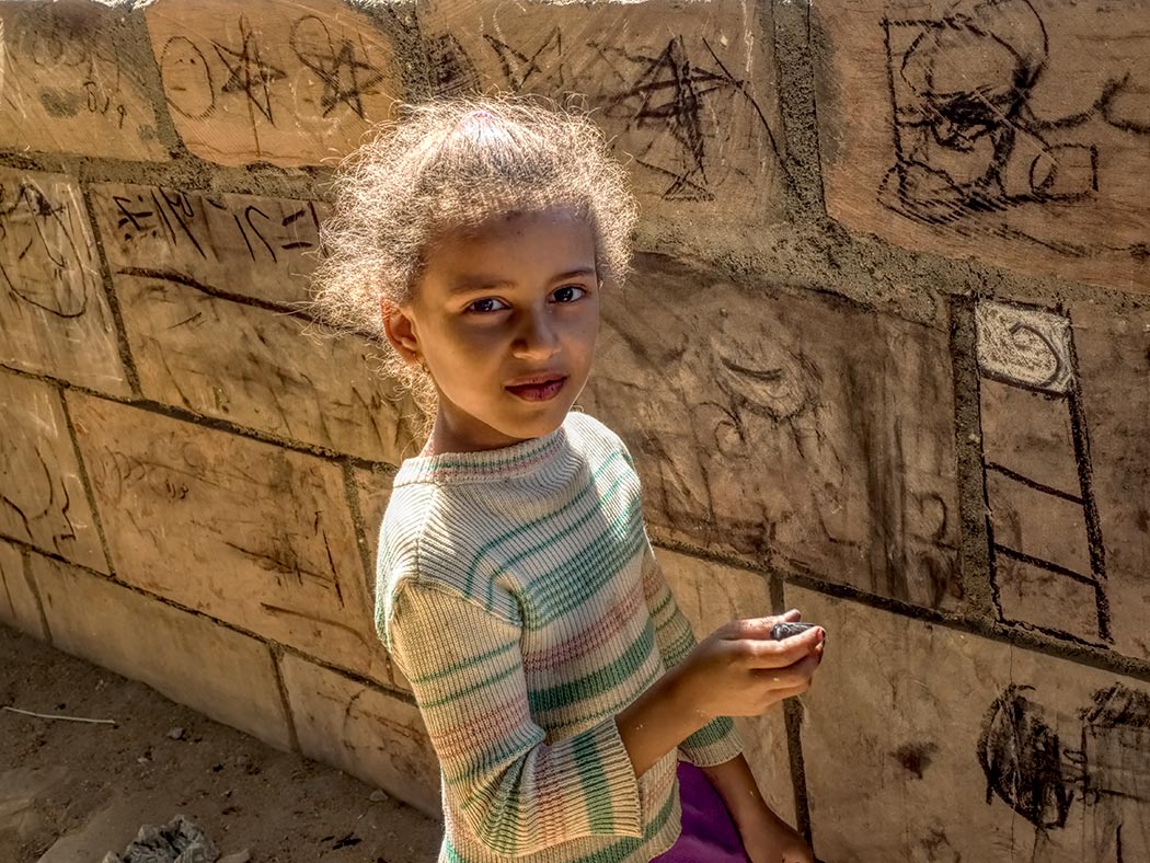 Young girl creates modern day hieroglyphics on a wall in the tiny village of El Kab, Egypt