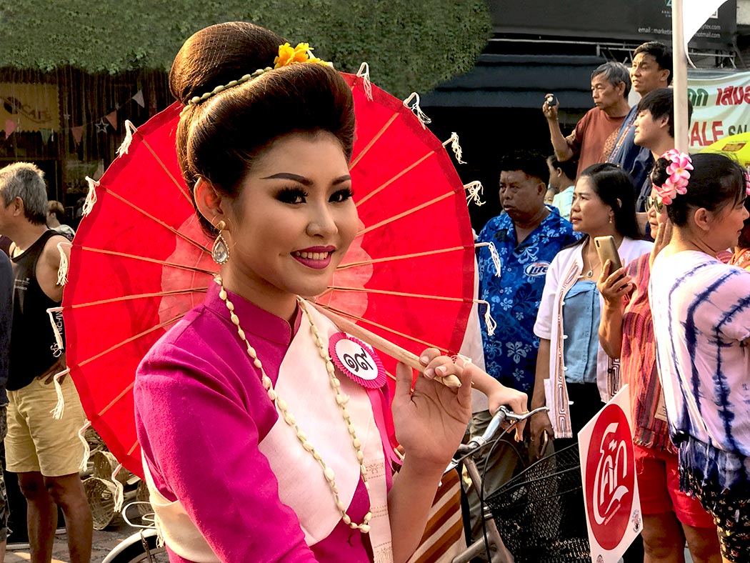 Thai women dressed in Lanna attire carry traditional paper umbrellas as they bicycle to Thapae Gate in the Old City of Chiang Mai, Thailand, during the Songkran Festival