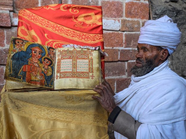 Ethiopia-Lalibela-Monastery-Church-of-Neakutoleab-priest-with-book Orthodox Christian priest at Monastery Church of Neakutoleab in Lalibela, Ethiopia, shows me 500-year oldMiracle of St. Mary book, printed on goatskin