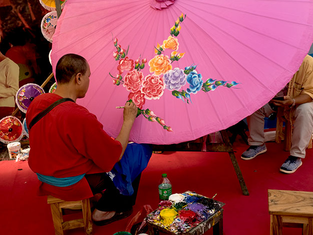 Artist paints a giant handmade paper umbrella at the Bo Sang Umbrella Festival