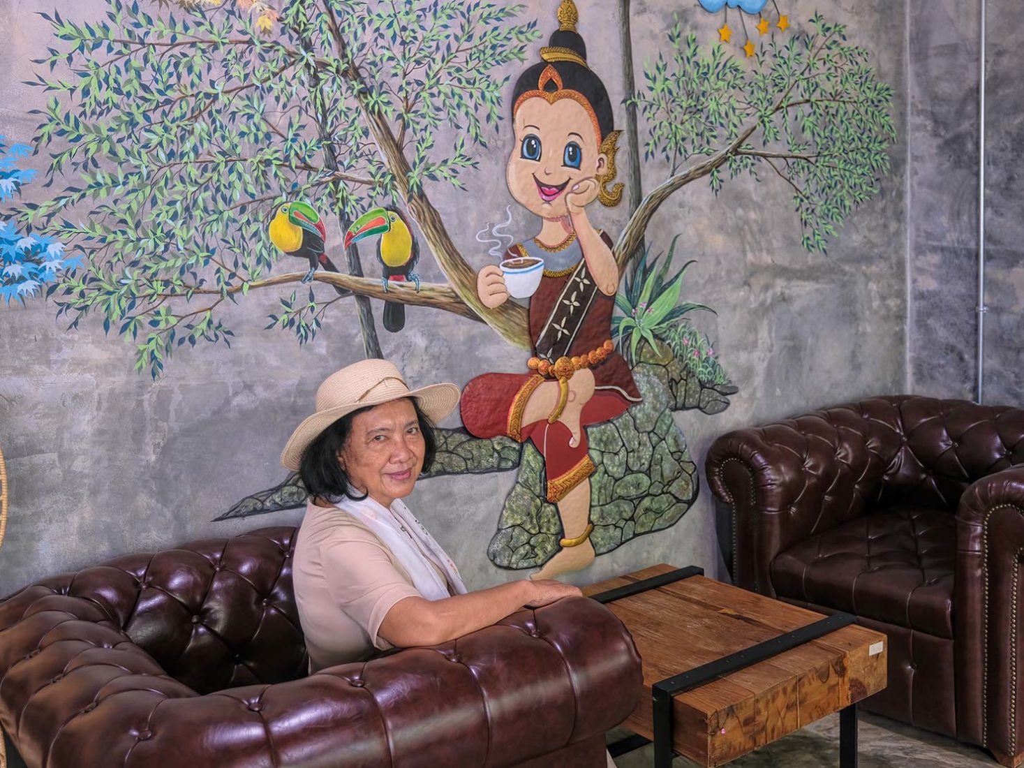 Mayuree in front of a Thai folk art painting in the coffee shop at Dantewada Land of Angels Waterfall Park