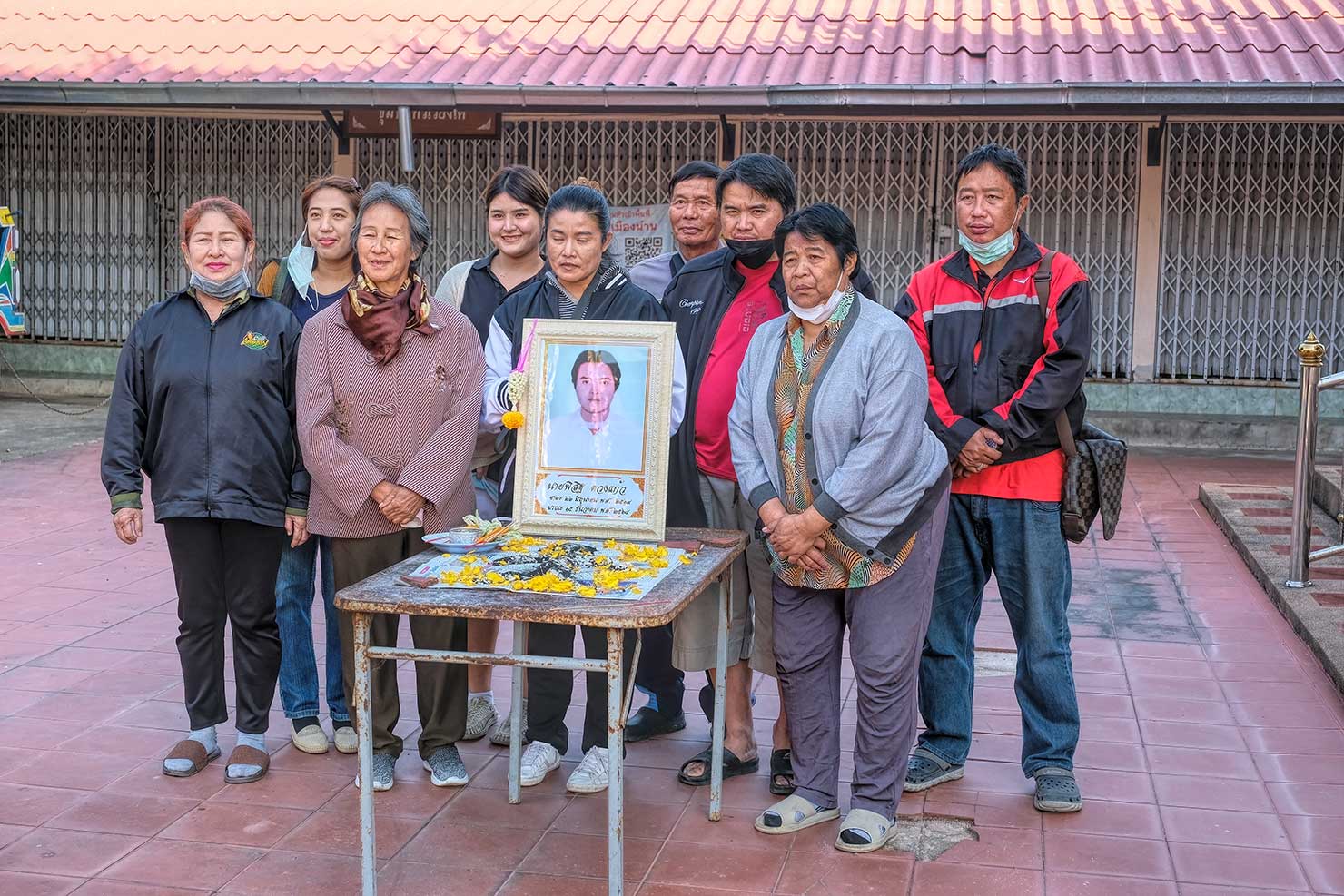March (center front, holding photo) and her family gather around a photo of her deceased brother, Phisit Duangkaew during his Buddhist funeral