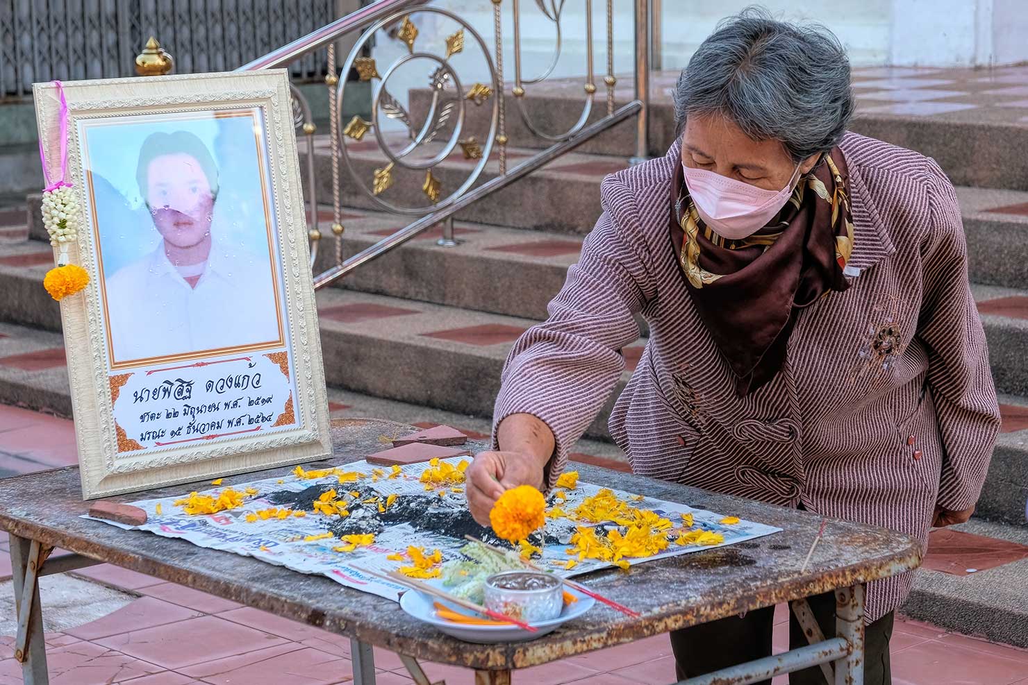 Family members sprinkle fresh flower petals atop the ashes