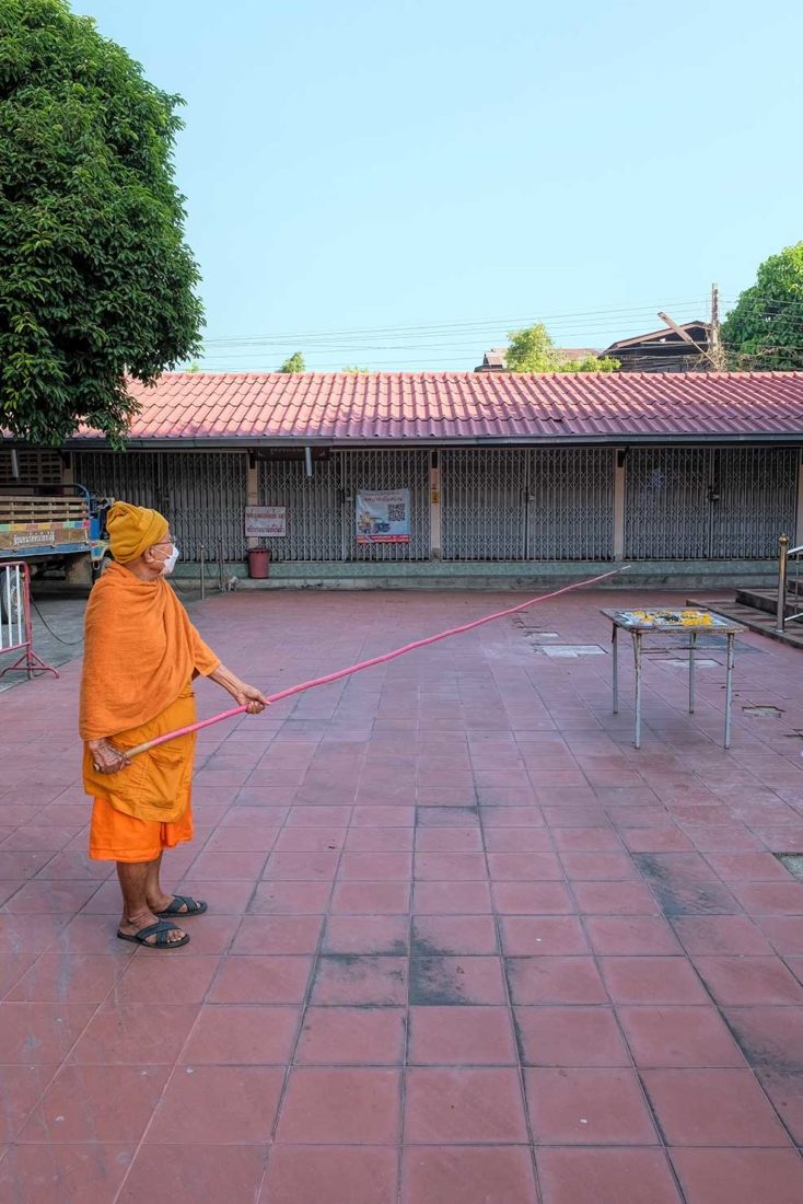 Monk lowers a long bamboo pole with a lit stick of incense tied to the top down to the figure made of ash and bone