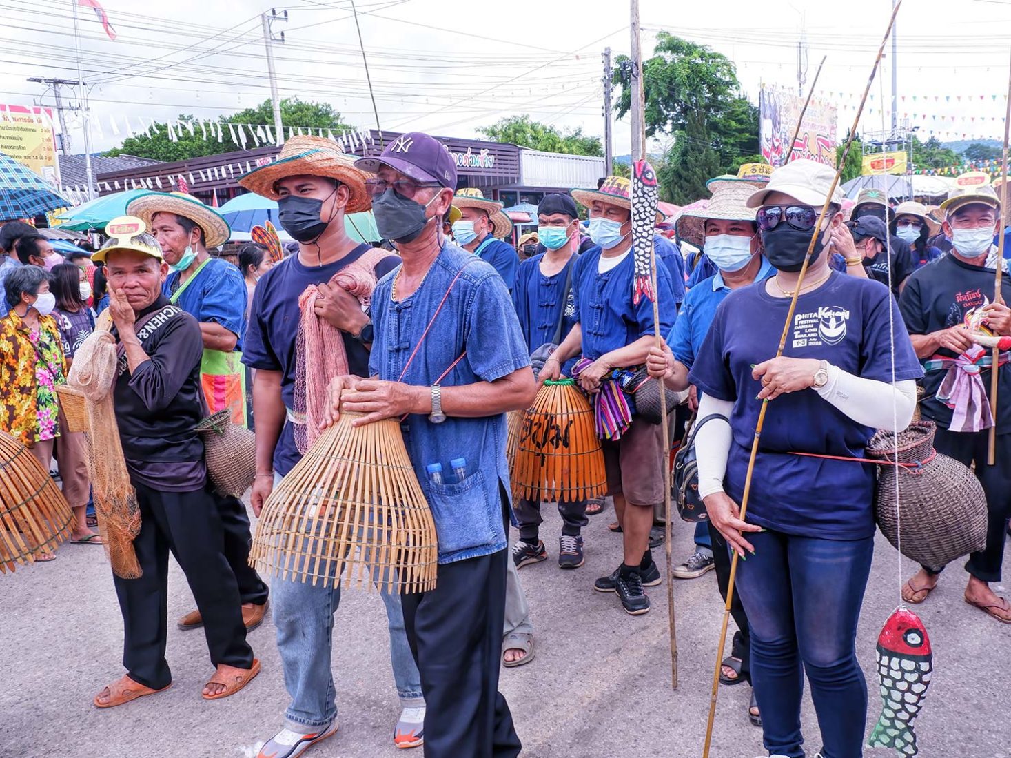 A group from one Tambon (district) in Loei wear traditional blue cotton Mor Hom attire and carry implements that represent their way of earning a living - chicken coop baskets and fishing poles