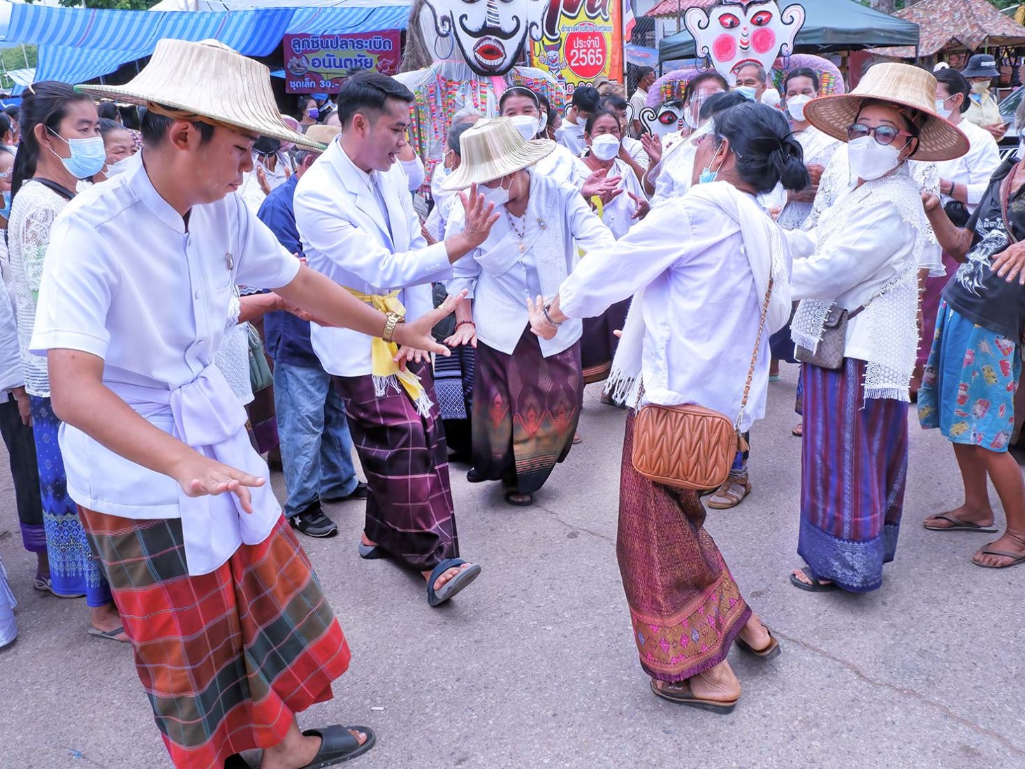 Group wearing traditional Pha Sin (woven wrap skirts) and bamboo hats dance in the street